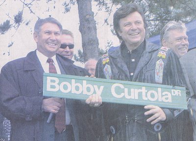 Thunder Bay Mayor Ken Boshcoff and Bobby hold a sign for Bobby Curtola Drive at Marina Park